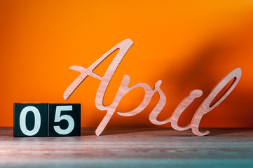 April 5th. Day 5 of month, daily wooden calendar on table with orange background. Spring time...