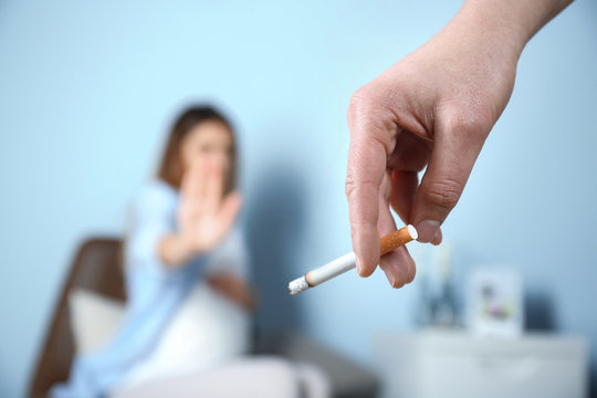 Hand with cigarette and blurred pregnant woman on background