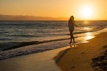 young girl is walking at sunset by the sea. Tourist girl on beach holiday. Happy girl running at sunset
