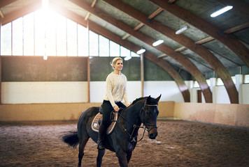 Blonde?female riding astride?on dark horse