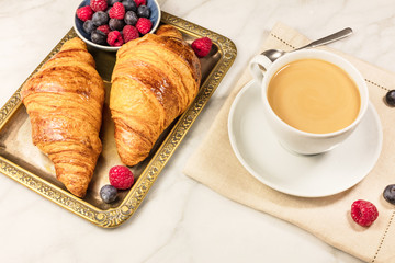 Cup of coffee with raspberries, blueberries, and croissants