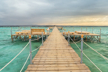 Obraz premium Pier with chaise longues in the sea in resort at sunset. Summer vacation. View at a clear sea with turquoise water. Summer vacation at a sea coastline in a exotic country.