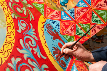 Hand of a sicilian cart painter while finishing some colored details.  Workshop of the sicilian folkloric craftsmanship Rosso Cinabro, Ragusa Ibla - obrazy, fototapety, plakaty