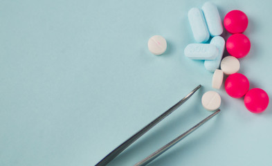 Health concept. various color pills and tweezers on blue background