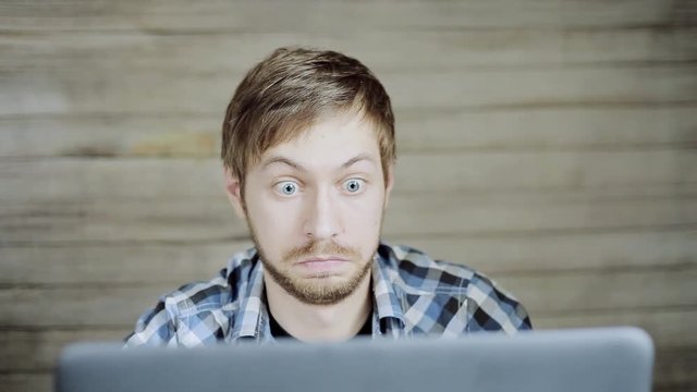 Young guy in blue shirt in front of the laptop very surprised
