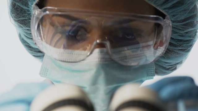 Lab scientist in goggles working with microscope, conducting medical research