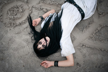Crazy young woman lying on sand with painted symbols and looking