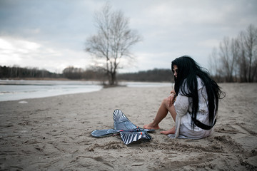 Crazy young woman sits on lake with kite on sand.