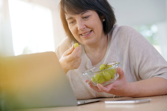 Woman Eating Grapes In Front Of Laptop