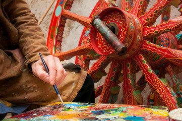 Hand of a sicilian cart painter while finishing some colored details of a wheel: workshop of the sicilian folkloric craftsmanship Rosso Cinabro, Ragusa Ibla