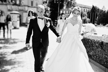 Fashionable wedding couple walking on streets of city at sunny wedding day.