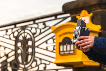 Making Vintage Vacation Pictures / Hand of unrecognizable woman hold an old camera in front of yellow antique german mailbox and ornamented handrail