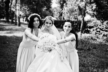 Bride posed on park with two cute brunette bridesmaids on pink dresses.