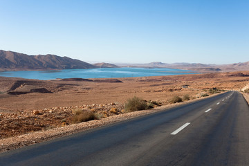 route droite au bord d'un lac au milieu d'un paysage aride