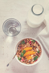 Healthy breakfast - milk, water and plate of granola with orange slices, mint and seeds, retro toned
