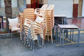 A pile of stacked chairs in front of a street cafe.