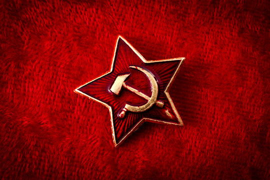 Old Soviet badge with the red star, a sickle and a hammer reminiscent of the cold war era worn by the soldiers of the red army on their hats, isolated on red velvet with a grungy aesthetic
