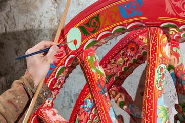 Hand of a sicilian cart painter while finishing some colored details of a wheel: workshop of the...