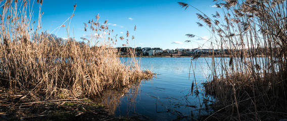 Wide angle, panorama photo of lake in spring - small private houses behind - blue sky and water 