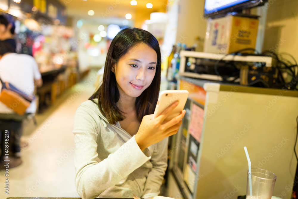 Wall mural Woman looking at mobile phone in japanese restaurant