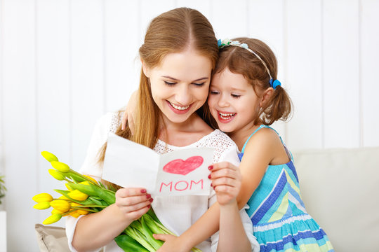 Happy mother's day! Child daughter congratulates moms and gives her a postcard and flowers
