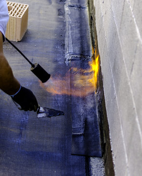 Roofer installing rolls of bituminous waterproofing membrane for the waterproofing of a terrace