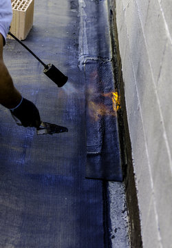 Roofer installing rolls of bituminous waterproofing membrane for the waterproofing of a terrace