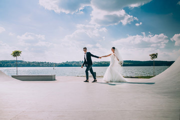 Fototapeta na wymiar Proud man walks behind pretty bride along the harbor over the sea