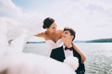 Elegant smiling young bride and groom walking on the beach, kissing and having fun, wedding...