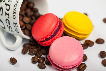 Colorful French delicious macaroons on coffee beans, cup with coffee beans on white background close up