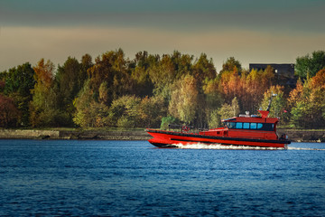 Red pilot ship moving past the autumn trees in Europe