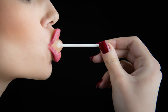 Juicy big lips of a young woman in profile suck a lollipop, nice long thin finger with red nail polish,isolated black background