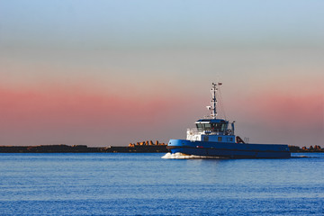 Blue small tug ship sailing past the breakwater dam in morning