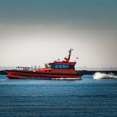 Red pilot ship moving at speed past the breakwater dam