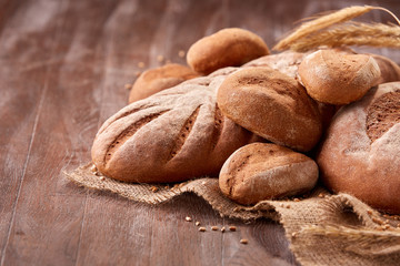 handmade tasty bread lying on burlap on the wooden table with flour, wheat and ears of wheat