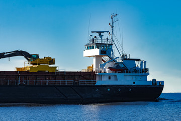 Obraz premium Black cargo ship with long reach excavator moving by Baltic sea