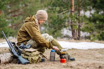 Papier Peint photo Lavable Chasser Female hunter preparing food with a portable gas burner in a winter forest.