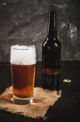 One open bottle of beer, a glass of beer, a foam. On a concrete background, copy space