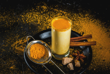 Obraz na płótnie Canvas Traditional Indian drink turmeric milk is golden milk with cinnamon, cloves, pepper and turmeric. On a concrete table, with spices on the background. In glasses, toned copy space