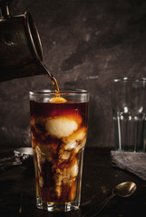 Cold coffee, frappe, frapuchchino. Affogato coffee with ice cream, On a concrete gray table. Toned, vintage. Coffee pot, spoon for ice cream, second glass. Smbd pours coffee. Vertical, copy space