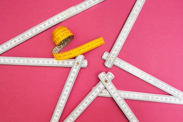 Folding ruler and measuring tape on a pink background.