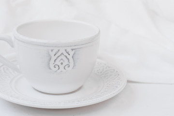 White relief ceramic tea cup with saucer on wood table cotton fabric, purity concept, minimalist, styled image for social media