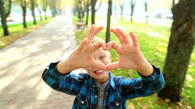 Funny kid of 9 year old makes shape of heart with hands, shows it into camera and looks through hole. Wide angle real time full hd video footage.