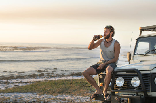 Man drinking beer while sitting on off-road vehicle at beach during sunset