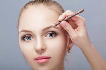 beautiful woman blonde uses professional pencil for eyebrow makeup.