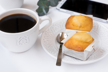 White cup with coffee, smartphone, pastry on plate, eucalyptus branch on table, business breakfast, feminine styled image for social media