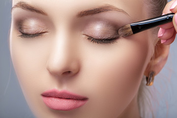 beautiful woman applying brown eye shadow using makeup brush. makeup for blue eyes - obrazy, fototapety, plakaty