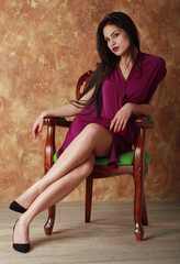 Beautiful girl in a burgundy dress sitting in a wooden chair.
