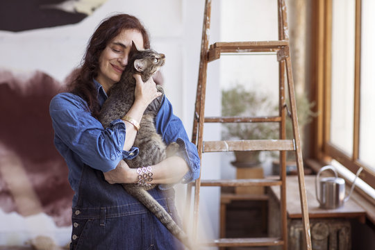 Smiling artist embracing cat while standing in workshop
