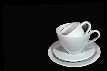 Different size of white porcelain coffee cups with saucers piled up on black background 